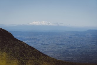 Snow-capped mountains on the horizon, hills in the foreground and blue sky, Mount Taranaki, New