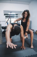 A personal trainer assists a man in a gym during a workout session, tarragona, spain