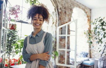 Young black woman wearing beige apron on flower shop background with copy space. Portrait of