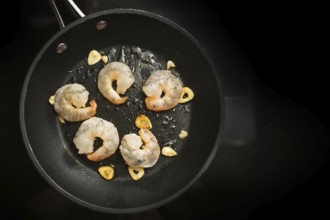Fresh shrimps are sauteed with garlic in olive oil in a cooking pan on the black stove, preparation