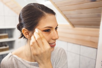 Beautiful young woman cleaning her face, removing make up with a cotton pad and micellar water.