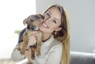 Pretty happy young woman with her pet dog held up to her cheek in her hands in a natural tender