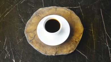 Overhead view of a coffee cup on a wooden coaster set on a dark marble table, ISTANBUL, TURKEY
