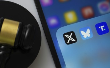 A close up of an iPad screen displaying the Truth Social, bluesky and X app alongside a judge's