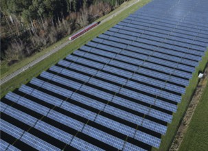 Red local railway runs on a non-electrified railway line next to a solar park through a green
