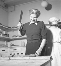 Happy woman in the kitchen in 1948. A woman in a restaurant kitchen stands and cuts the meat into