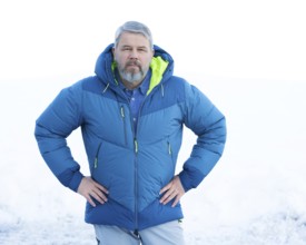 Man, 56 years old with grey hair and a full grey beard standing in front of a snowy area in winter,