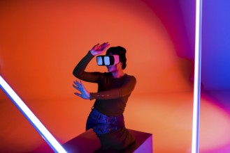 Happy female in VR headset smiling and exploring virtual reality under red neon illumination in