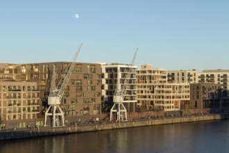 Weather, winter, moon, walkers and historic harbour cranes in front of modern architecture in the