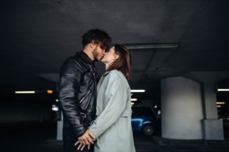 The couple shares a kiss in a dimly lit parking garage, showing intimacy and connection