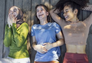 Multiracial young teen female friends resting in the park after sport training laughing and having