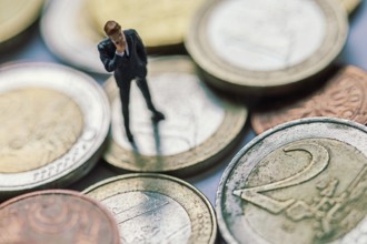 Figure of a thoughtful businessman between euro coins, studio shot, Germany, Europe
