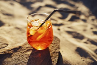 Orange slice and aperol spritz cocktail on a stone against the backdrop of a sandy beach. Glass