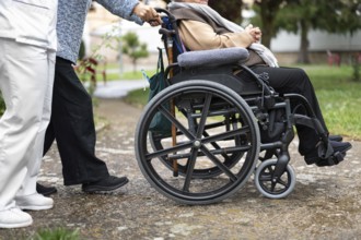 Senior woman in wheel chair with relative and nurse caregiver, outdoors at nursing home garden.