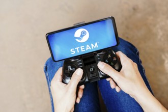 In this photo illustration, a person playing on a joystick and the Steam logo displayed on a