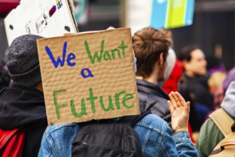 A cardboard sign is viewed close-up saying we want a future as a crowd of environmental campaigners