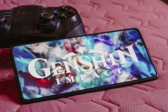 In this photo illustration, the Genshin Impact logo is displayed on a smartphone screen, next to a