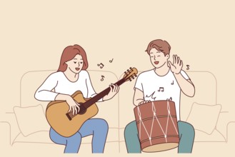 Cheerful friends man and woman playing musical instruments, sitting on sofa and using drum with