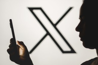 In this photo illustration, a woman's silhouette holds a smartphone with the Twitter (X) new logo