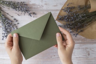 Flat lay composition of female hands holding green envelope with dry lavender flowers. Copy space