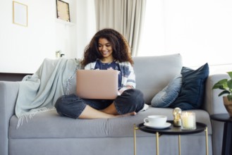 Excited cheerful young black woman using laptop computer on sofa at home, getting good news,