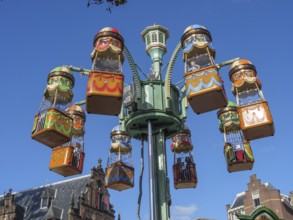 Colourful carousel cabins in an amusement park in front of historic buildings under a clear sky,
