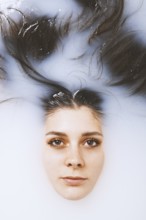 beauty portrait of young woman face and brunette long hair floating in milk bath