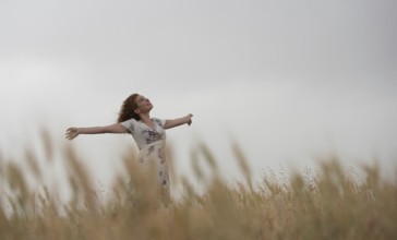 Happy woman in a floral dress stands amidst golden wheat, enjoying the serene landscape