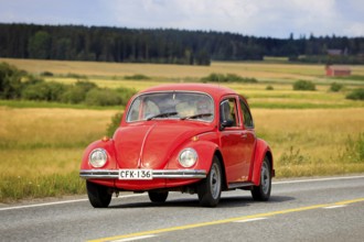 Red Volkswagen Beetle, officially Volkswagen Type 1, driving along country road on Maisemaruise