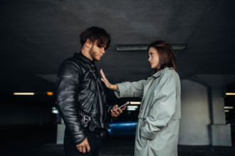 A man and woman face each other in an underground parking garage, the atmosphere tense