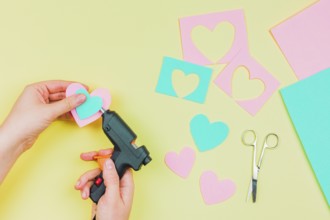 Close up woman s hand sticking paper heart shape with electric hot glue gun