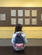 Back view of teen girl with backpack in museum visiting exhibition, schoolgirl sitting on bench in