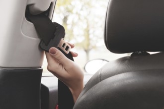 A woman's hand reaches behind her seat belt to fasten it. The concept of safe driving of women by