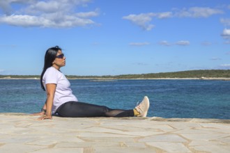 Woman sitting by the ocean, wearing sunglasses, beautiful latina woman by the sea in Colonia San