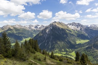 Panorama of impressive, snow-covered Alpine mountains, above a green valley under sun and clouds in