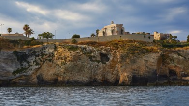Building on a cliff under a cloudy sky next to the sea, boat trip around the island of Ortigia,