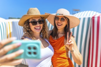Two cheerful women wearing stylish sunglasses and trendy sun hats are capturing a joyful selfie on