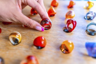 Woman's hand with pink nail polish picking up a colorful resin ring from a wooden display at a