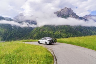 The car parked on a path in an impressive mountain landscape with fog and grass, electric car on