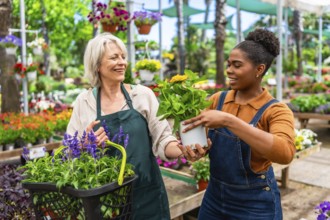 Two female florists or gardeners are smiling and holding plants and flowers in a greenhouse or