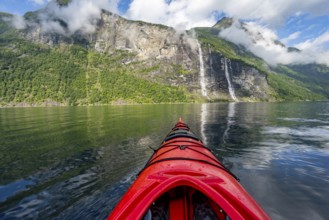 Kayak trip on the Geirangerfjord with waterfall The Seven Sisters, tip of a red kayak in the fjord,