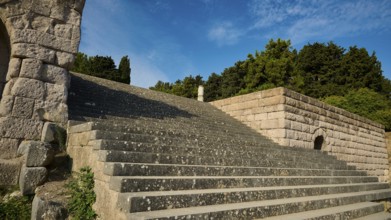 Stone staircase next to old walls, surrounded by nature and trees, open staircase to the second