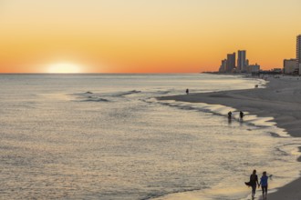 People walking and playing on the beach as the sun sets over the Gulf of Mexico at Gulf Shores,