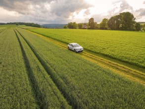 Car on a rural road with fields and rooftops under a cloudy sky, Deer E- CarSharing, Renault Megane