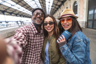 Three cheerful young tourists taking a selfie at the train station, excited for their upcoming