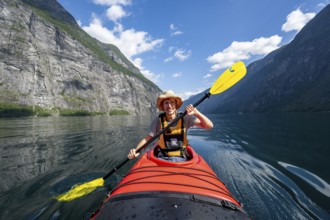Kayak trip on the Geirangerfjord, young man paddling in red kayak, atmospheric fjord landscape,