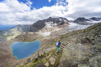 Mountaineer on hiking trail in front of dramatic high mountain landscape, view of mountain lake