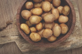 A bowl filled with small, freshly harvested potatoes sits on a rustic wooden cutting board,