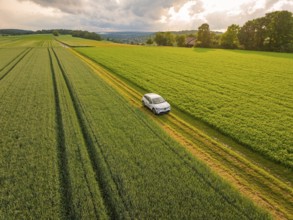 A car on a farm track between green meadows and under drifting clouds, Deer E- CarSharing, Renault
