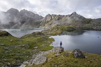 Mountaineer on a rock in front of mountain lakes Wangenitzsee and Kreuzsee, cloudy mountain peaks